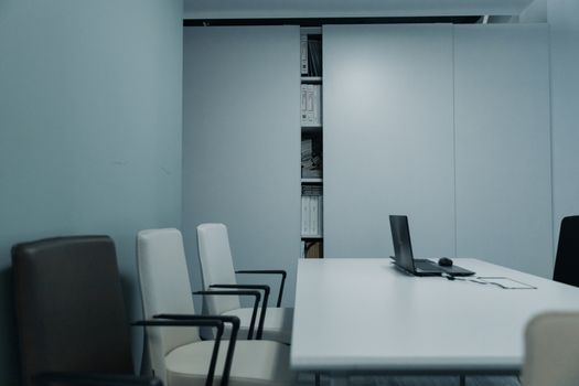 A sleek conference room with a white table and chairs, featuring a laptop on the table.