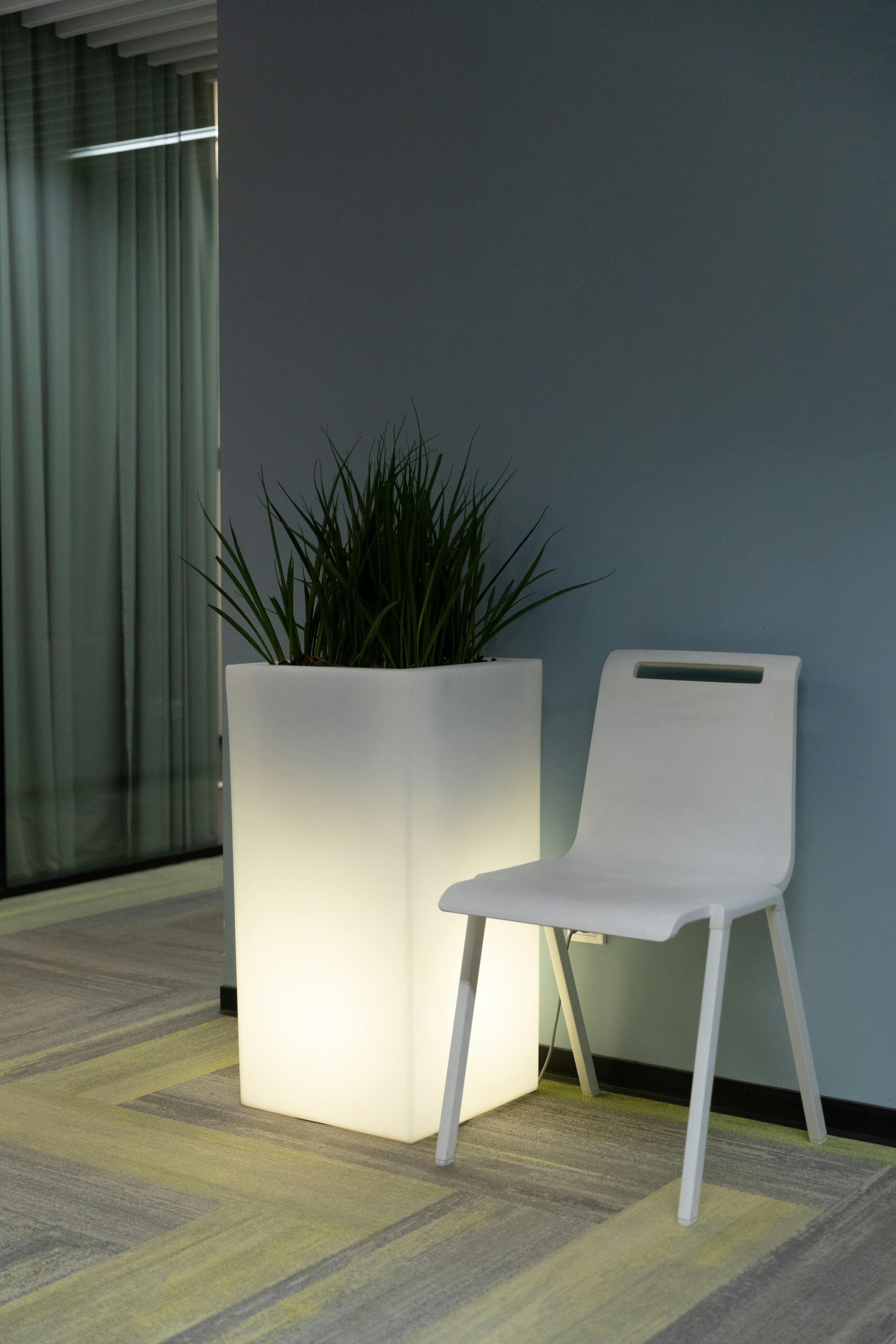Free A contemporary minimalist interior featuring a white chair and an illuminated lamp with green plant. Stock Photo