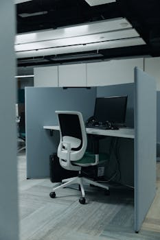 An empty modern office cubicle with a computer and swivel chair ready for work.