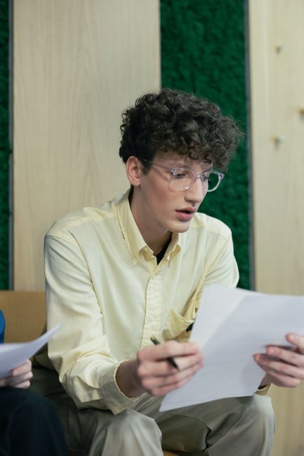 Young adult man engaged in reading and writing while seated indoors, showing concentration and focus. Young adult man engaged in reading and writing while seated indoors, showing concentration and focus.