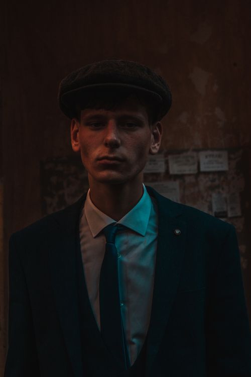 Free A serious man wearing an ivy cap and suit captured in a moody, dark setting. Stock Photo