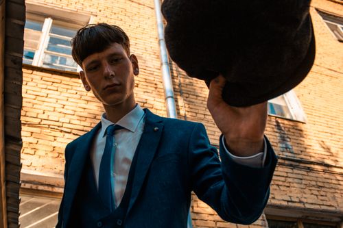 Free Stylish young man in a blue suit holds a beret on a city street with a brick backdrop. Stock Photo