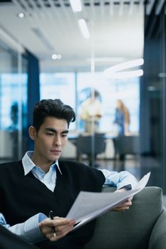 Young professional reading paperwork in a modern office setting.