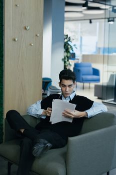 Businessman reading paperwork while sitting in a modern office.