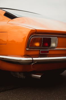 Close-up of a vintage orange car's rear end showcasing shiny chrome details, highlighting classic design.