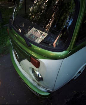 A retro Volkswagen van with a magazine on the dashboard, parked outdoors.