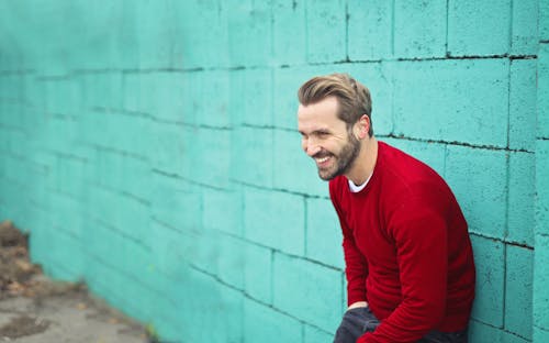 Kostenlos Mann, Der Einen Roten Pullover Trägt, Der An Einer Blauen Wand Lehnt Stock-Foto