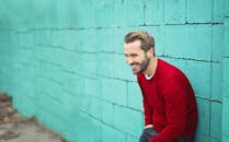 在布达佩斯，一名穿着红色毛衣的男子面带微笑，倚靠在青色砖墙上，散发着幸福的气息