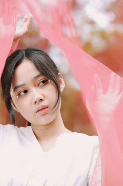 Stunning portrait of a young woman gracefully posing with flowing pink fabric outdoors.