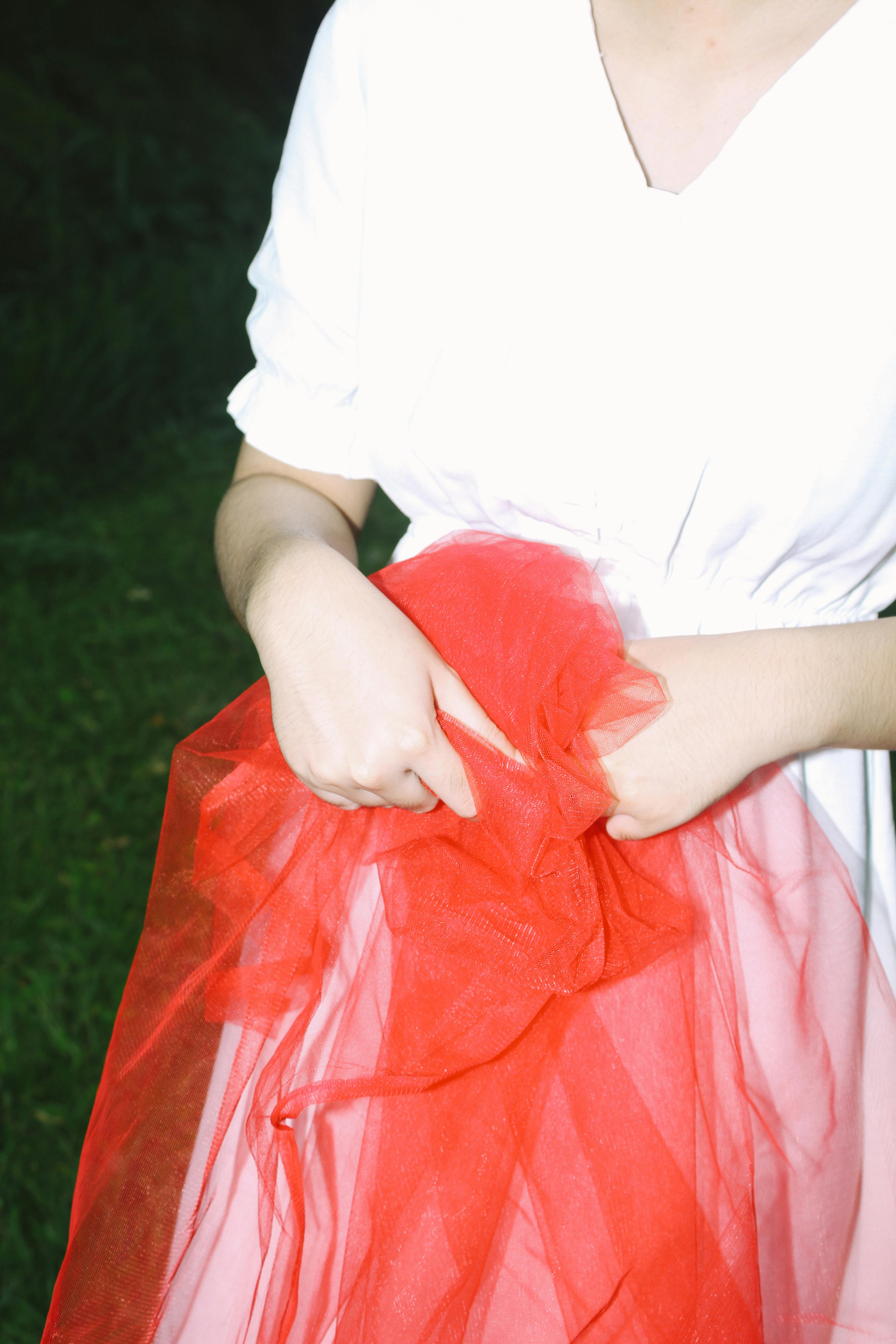 A close-up of a woman in a white dress holding vibrant red fabric outdoors.