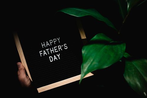 Free Dark background with Happy Father's Day sign held by a hand next to green leaves. Stock Photo