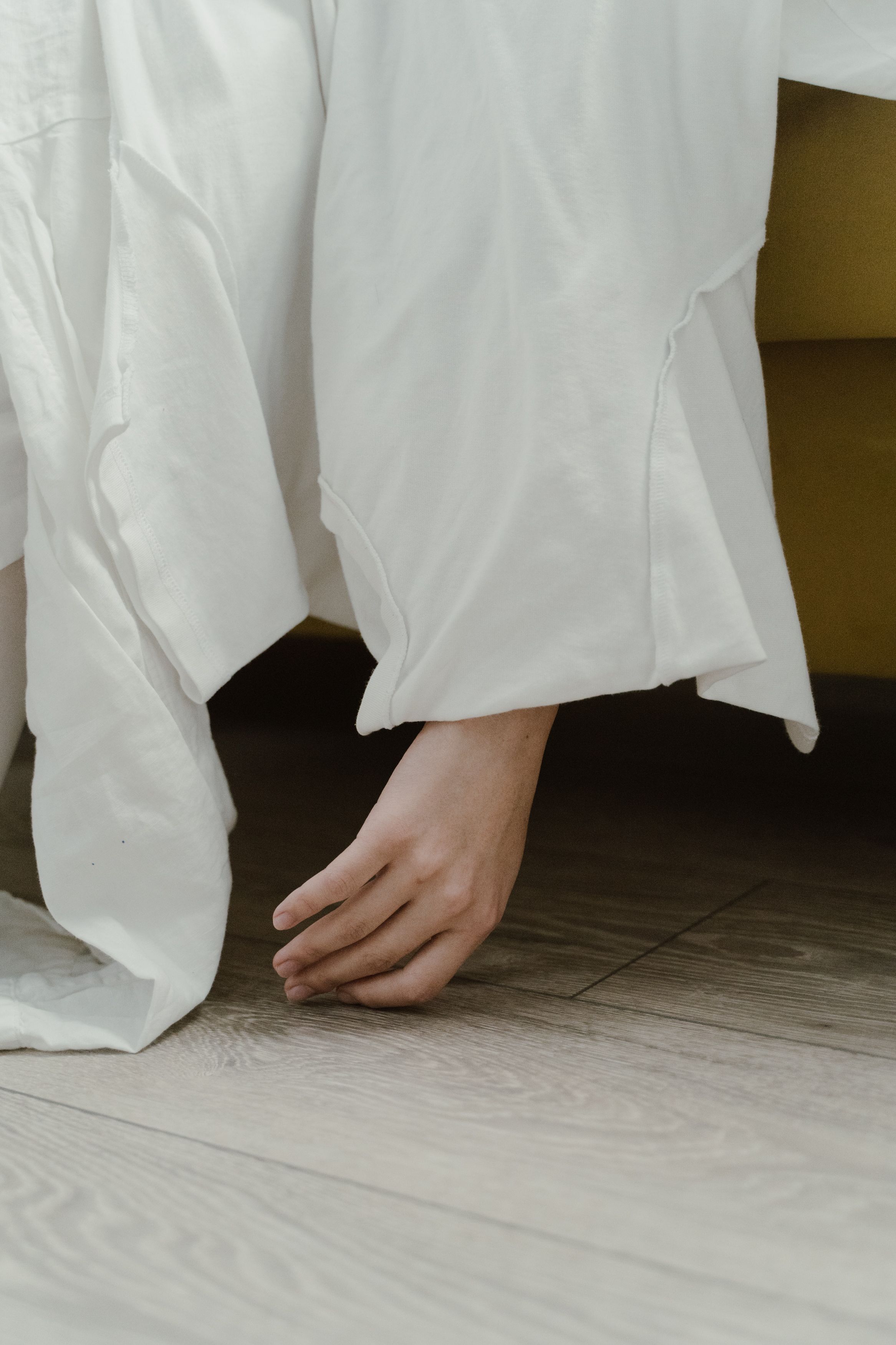 Artistic composition featuring a hand draped over white fabric against a wooden floor.