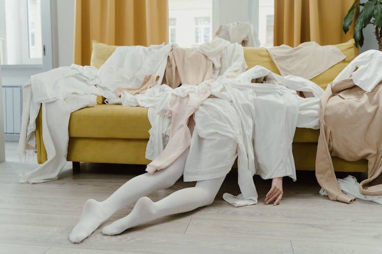 Person Lying Down On The Couch Covered With Clothes 