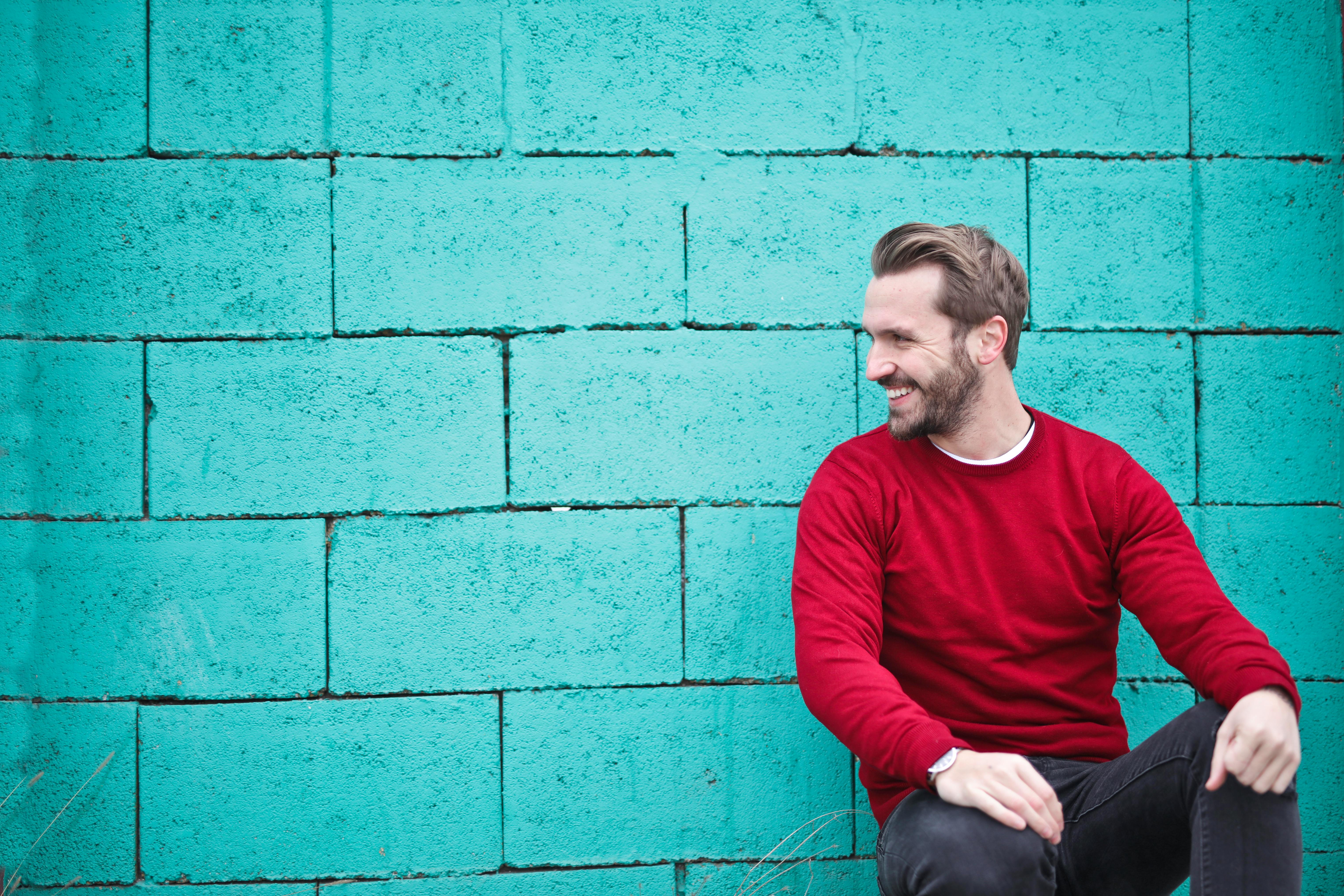 man wearing red sweatshirt and black pants leaning on the wall