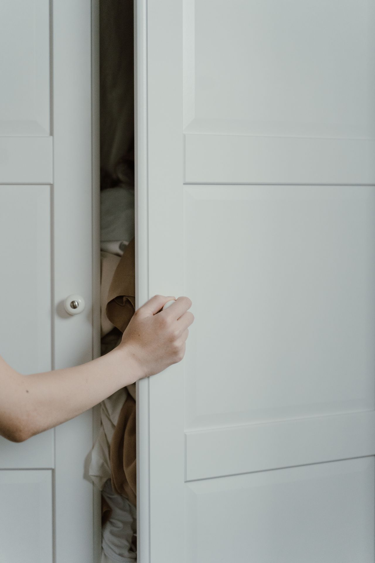 A hand opening a white wardrobe door by its round knob