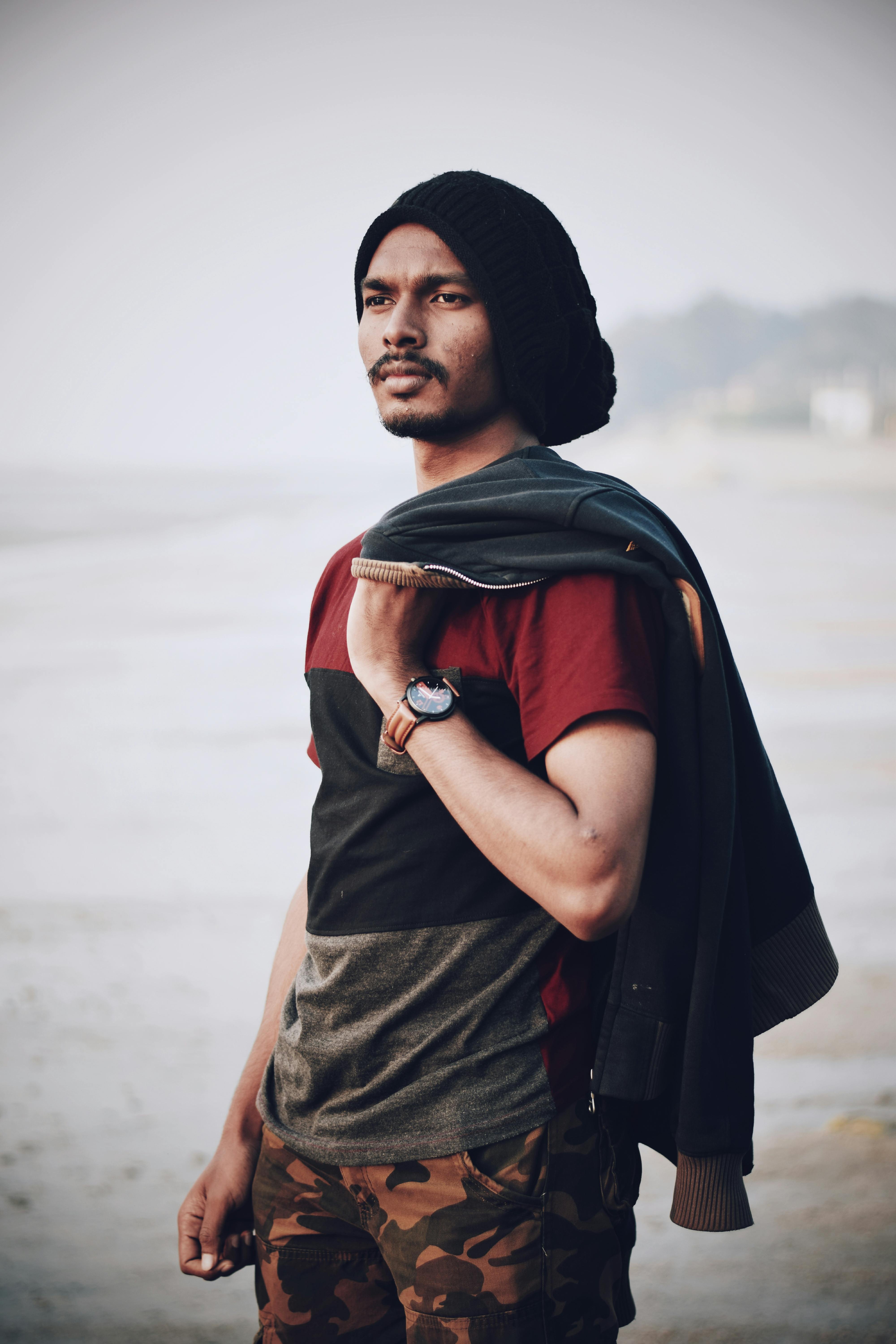 白天，一位戴着无檐帽、穿着夹克的时尚男子在昌迪普尔海滩上摆姿势