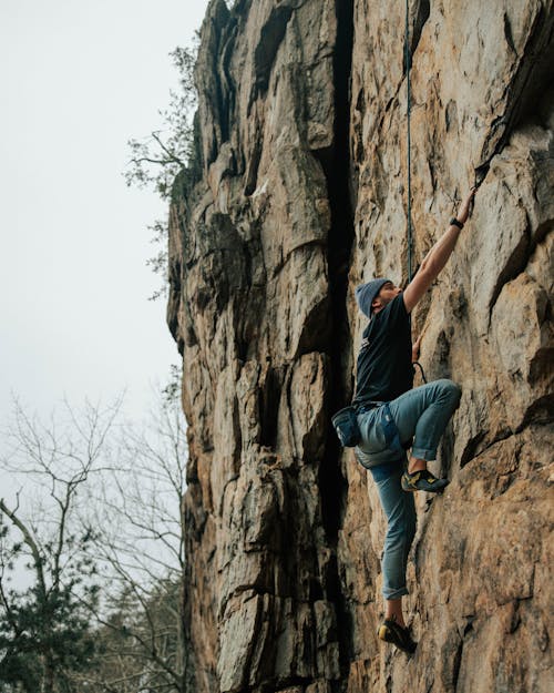 Man in Black T-shirt and Blue Denim Jeans Climbing on Rock Formation