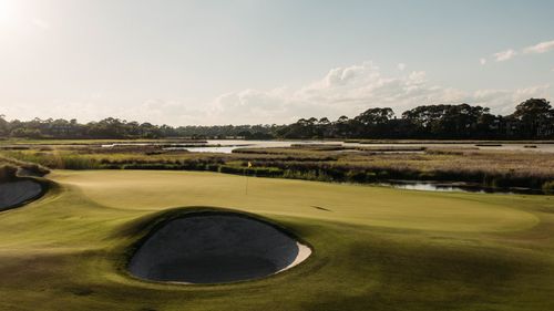Free A picturesque view of a golf course in Kiawah Island, SC, showcasing lush greens, water features, and a serene sunset. Stock Photo