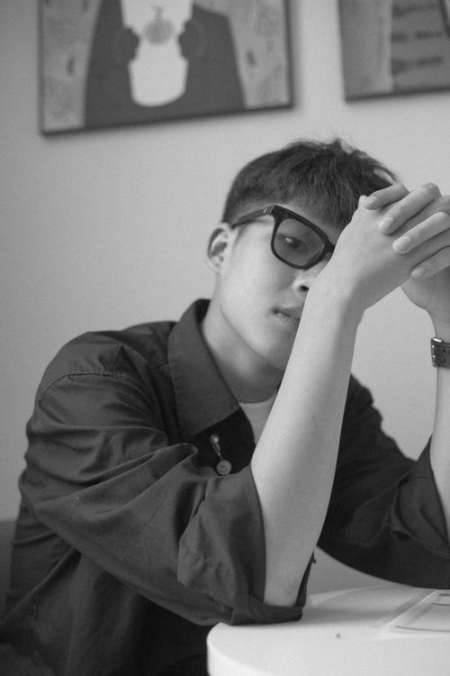 Free Grayscale portrait of a man wearing glasses, seated with hands together, in a thoughtful pose indoors. Stock Photo
