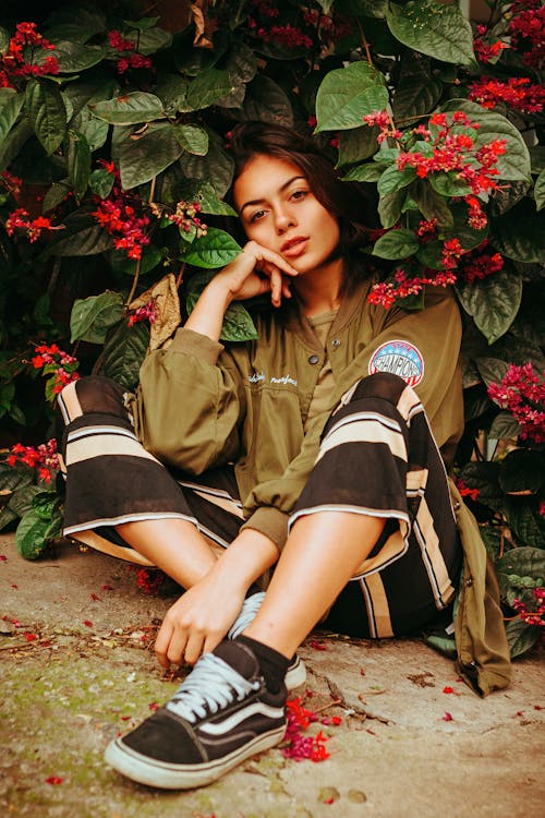 Young Woman in Striped Pants Sitting on the Ground Beside Red Blossom Tree