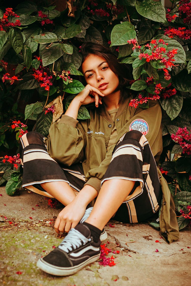 Young Woman In Striped Pants Sitting On The Ground Beside Red Blossom Tree