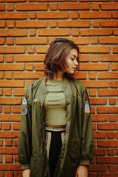 Young Woman in Khaki Coat Standing Beside Brick Wall