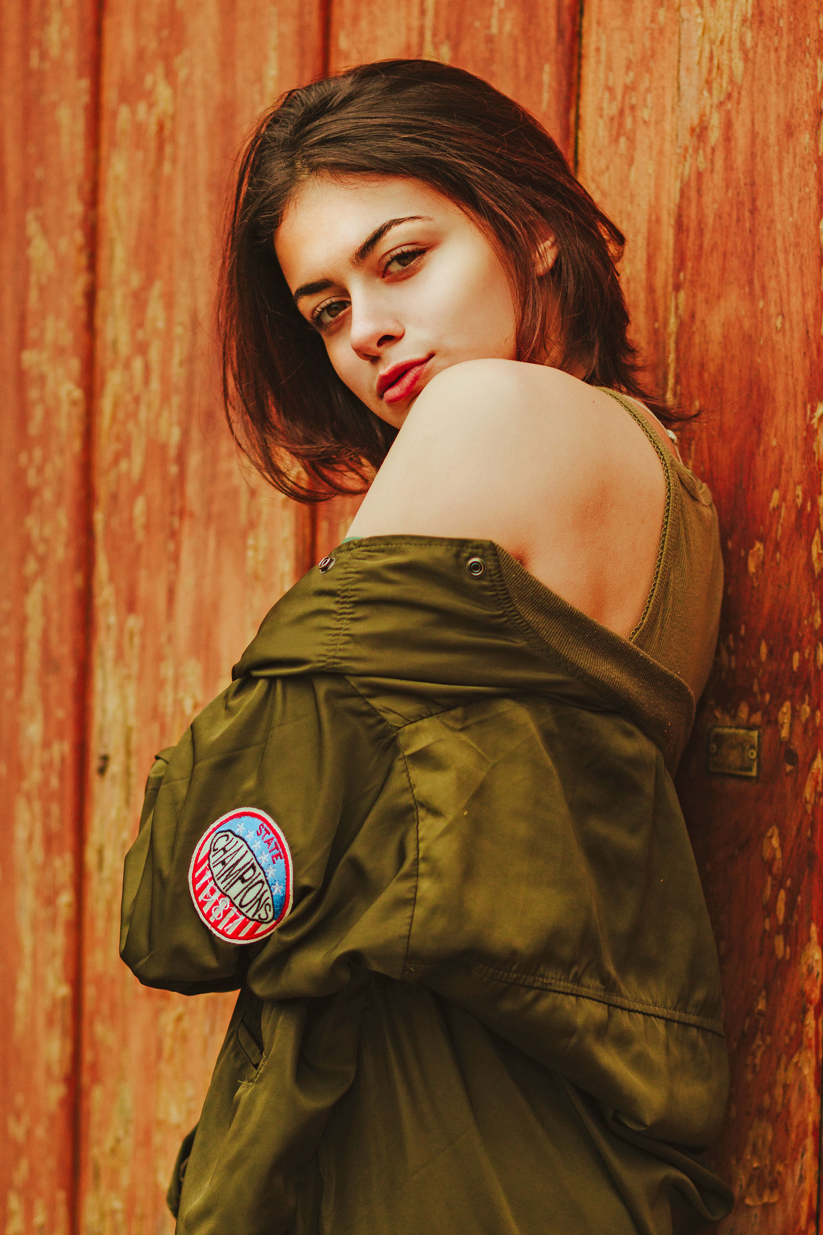 Portrait of a confident woman standing against a wooden backdrop wearing a stylish green jacket.