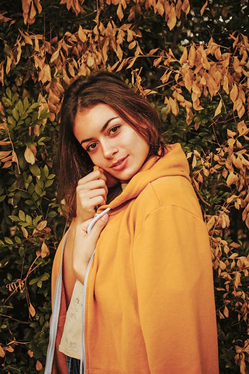 Woman in Yellow Coat Smiling While Standing Near Tree