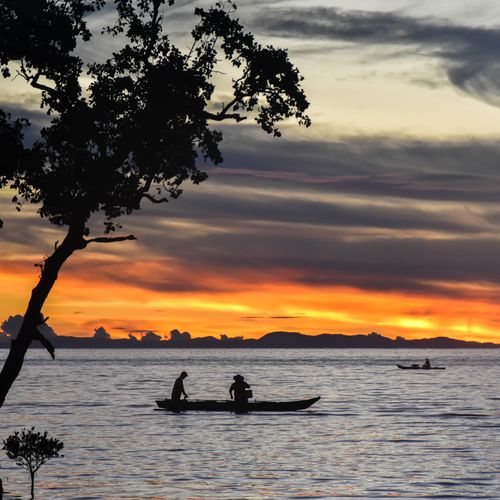 Free Silhouette of fishermen on boats during a vibrant ocean sunset with dramatic clouds. Stock Photo