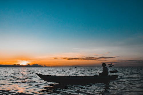 Silhouette of a Man in a Boat in the Sea During Sunset
