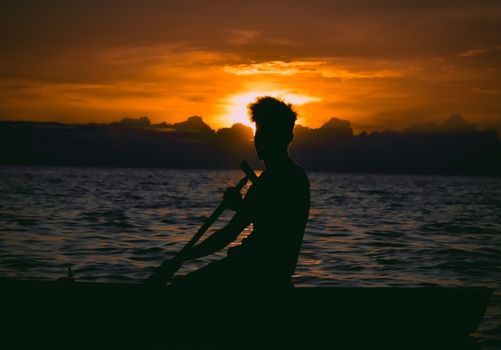 A scenic silhouette of a man paddling a boat at sunset with a dramatic sky backdrop.