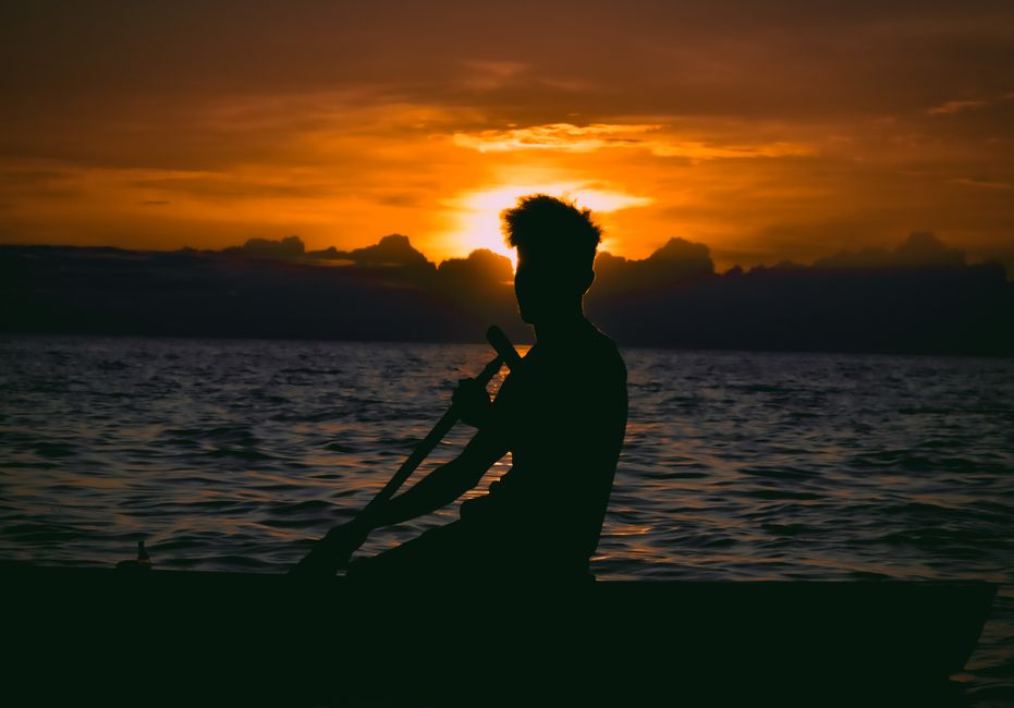 A scenic silhouette of a man paddling a boat at sunset with a dramatic sky backdrop.