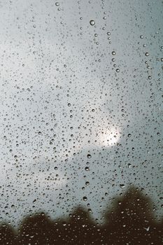 Raindrops resting on a glass window with a view of a cloudy, overcast sky.