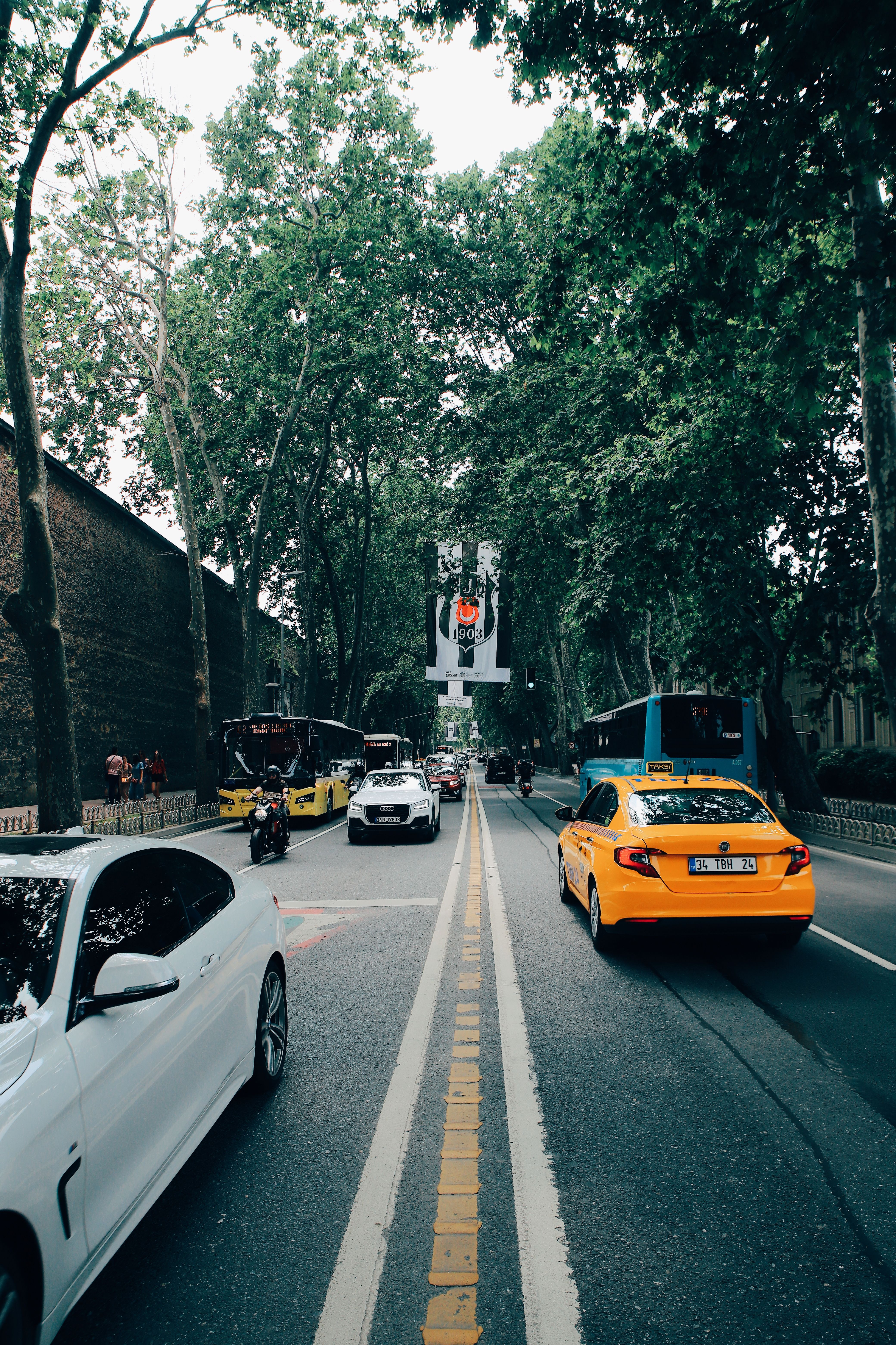 A bustling city street lined with cars and lush trees under clear daylight, offering a vibrant urban scene.