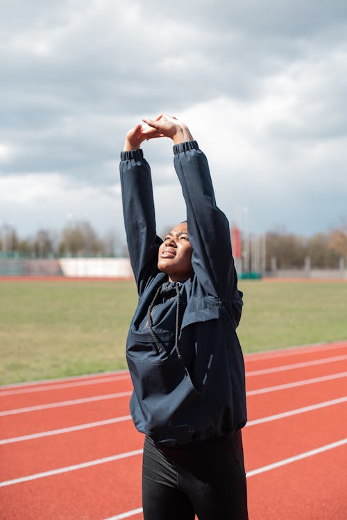 Free Woman in Black Hoodie Stretching on Track and Field Stock Photo