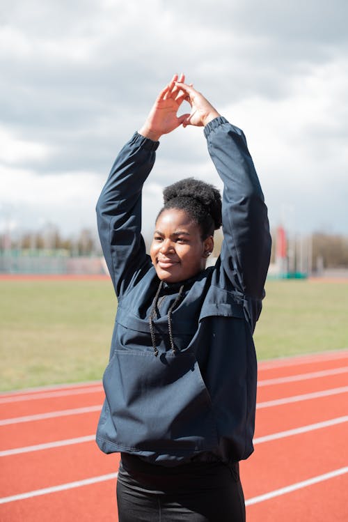 Free Woman Smiling While Standing on Track and Field with Raised Hands Stock Photo