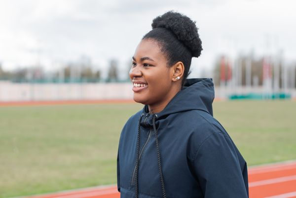 Smiling woman in a black jacket on an outdoor running track — photo by Mikhail Nilov on Pexels