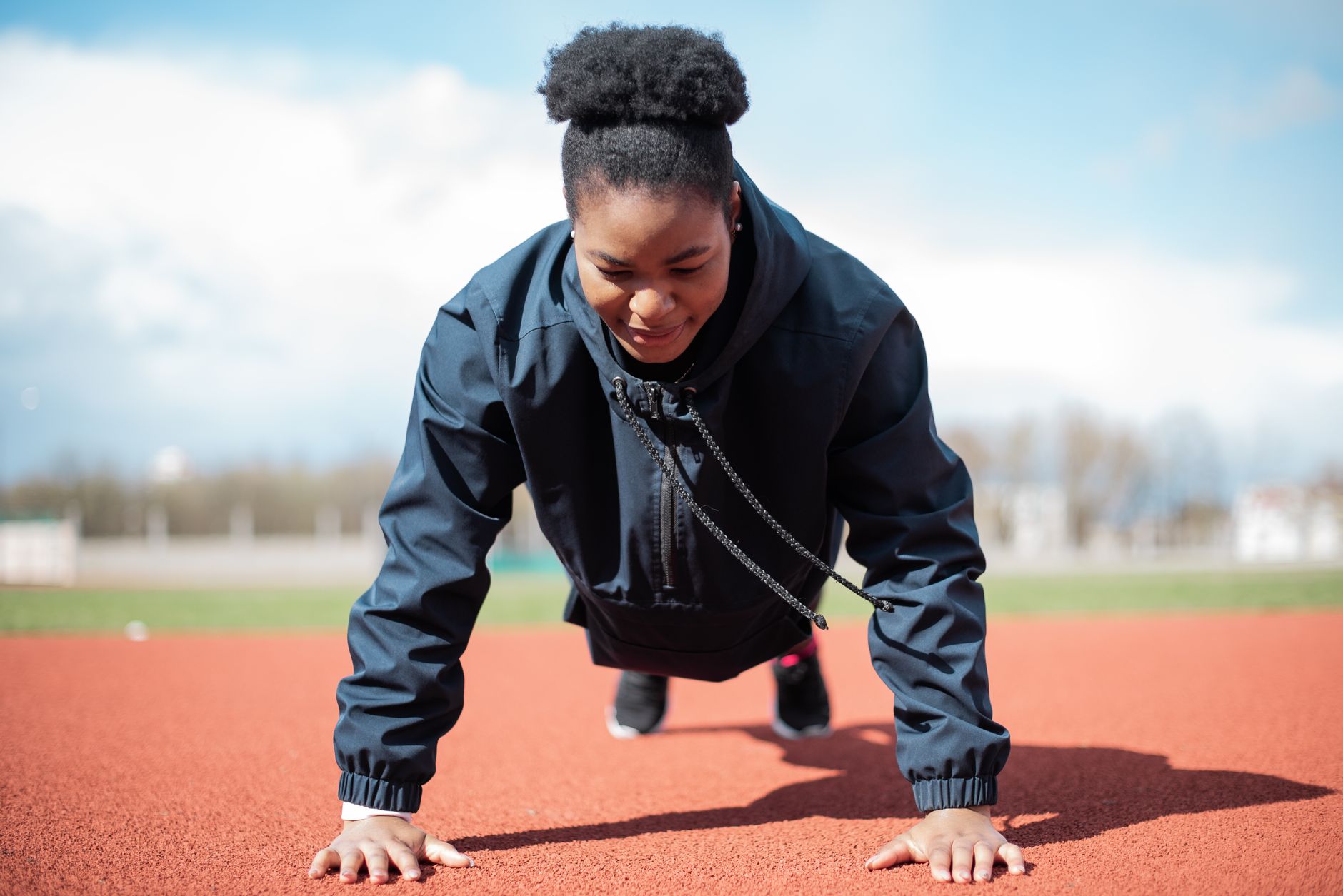 An African American woman performing push-ups on a track, promoting fitness and healthy lifestyle.