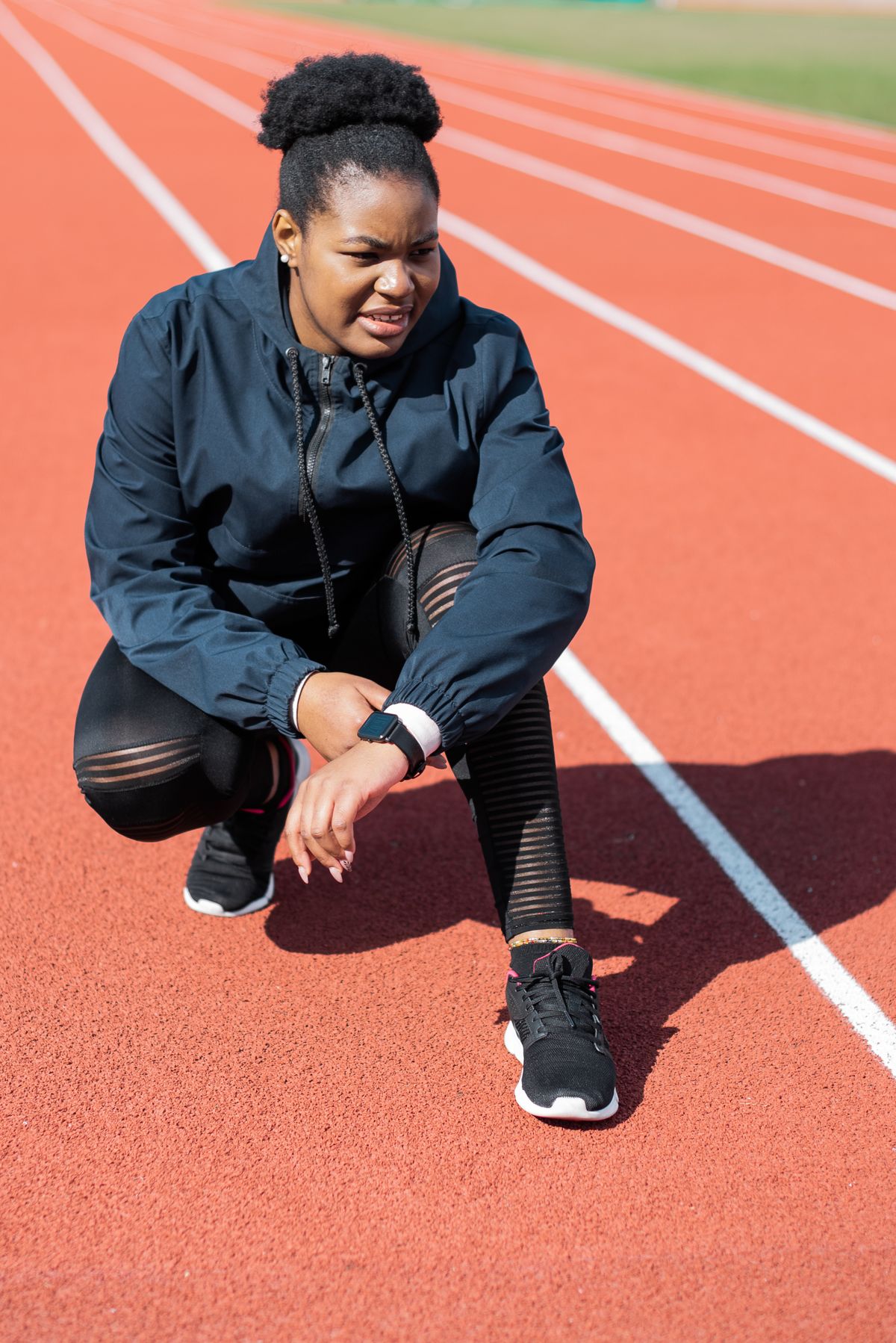Athlete in jacket and leggings resting on an outdoor running track