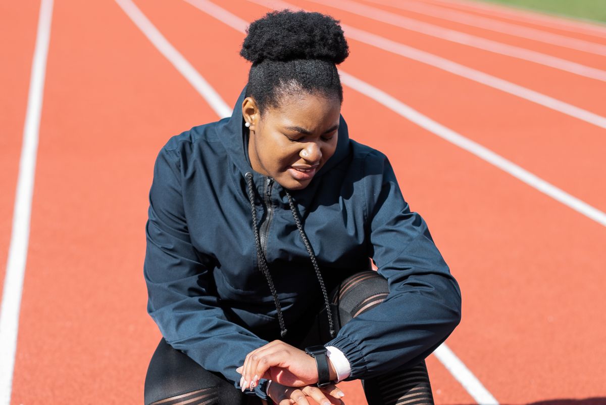 Woman in performance activewear checking her smartwatch on a running track