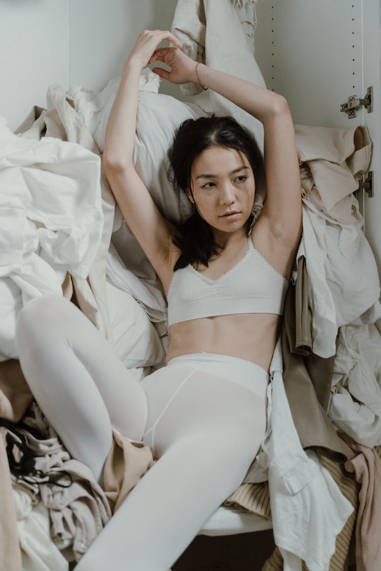 A Woman Sitting On Dumped Clothes Inside A Closet