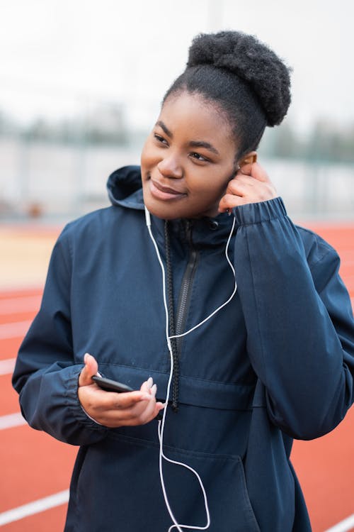 Free A Woman in Blue Jacket Listening to Music Using an Earphone Stock Photo
