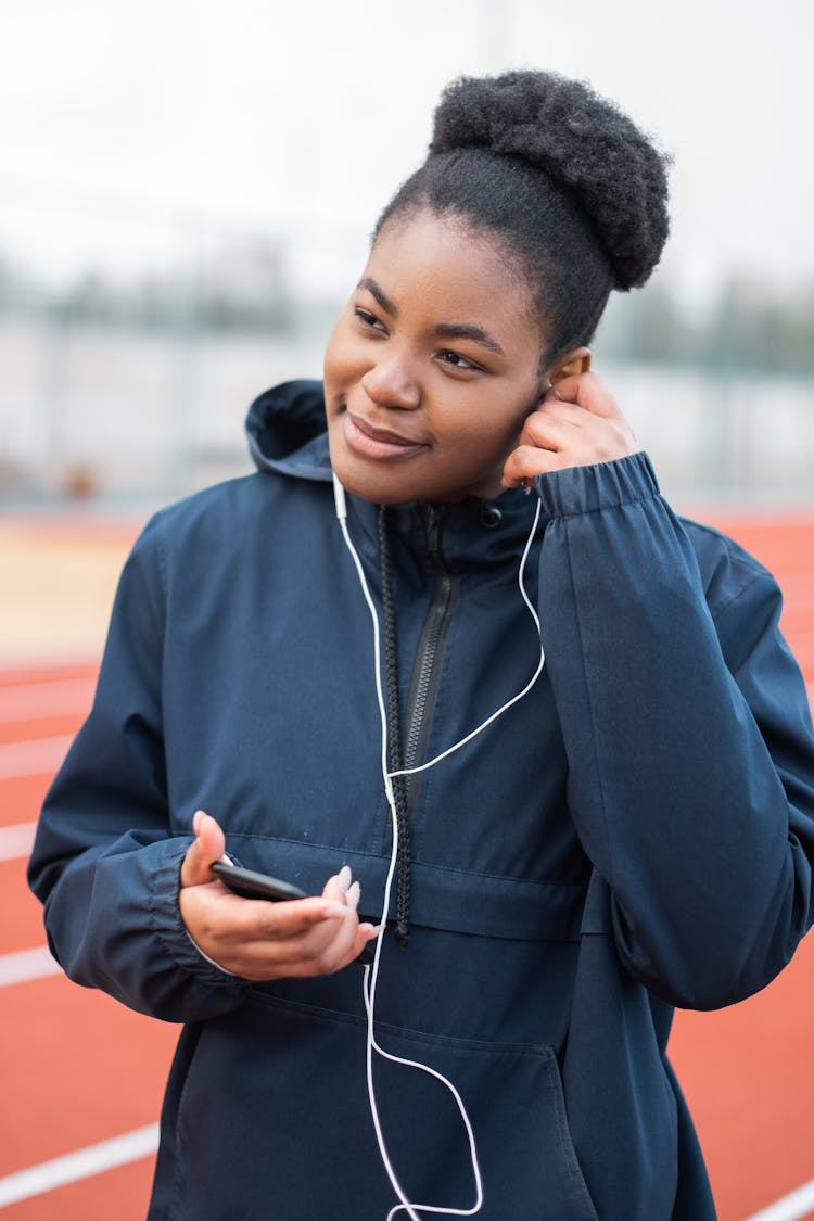 A Woman In Blue Jacket Listening To Music Using An Earphone