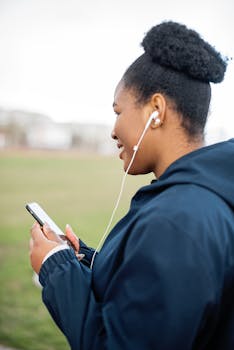Side view of a young woman with earbuds enjoying music on her phone in a park setting.