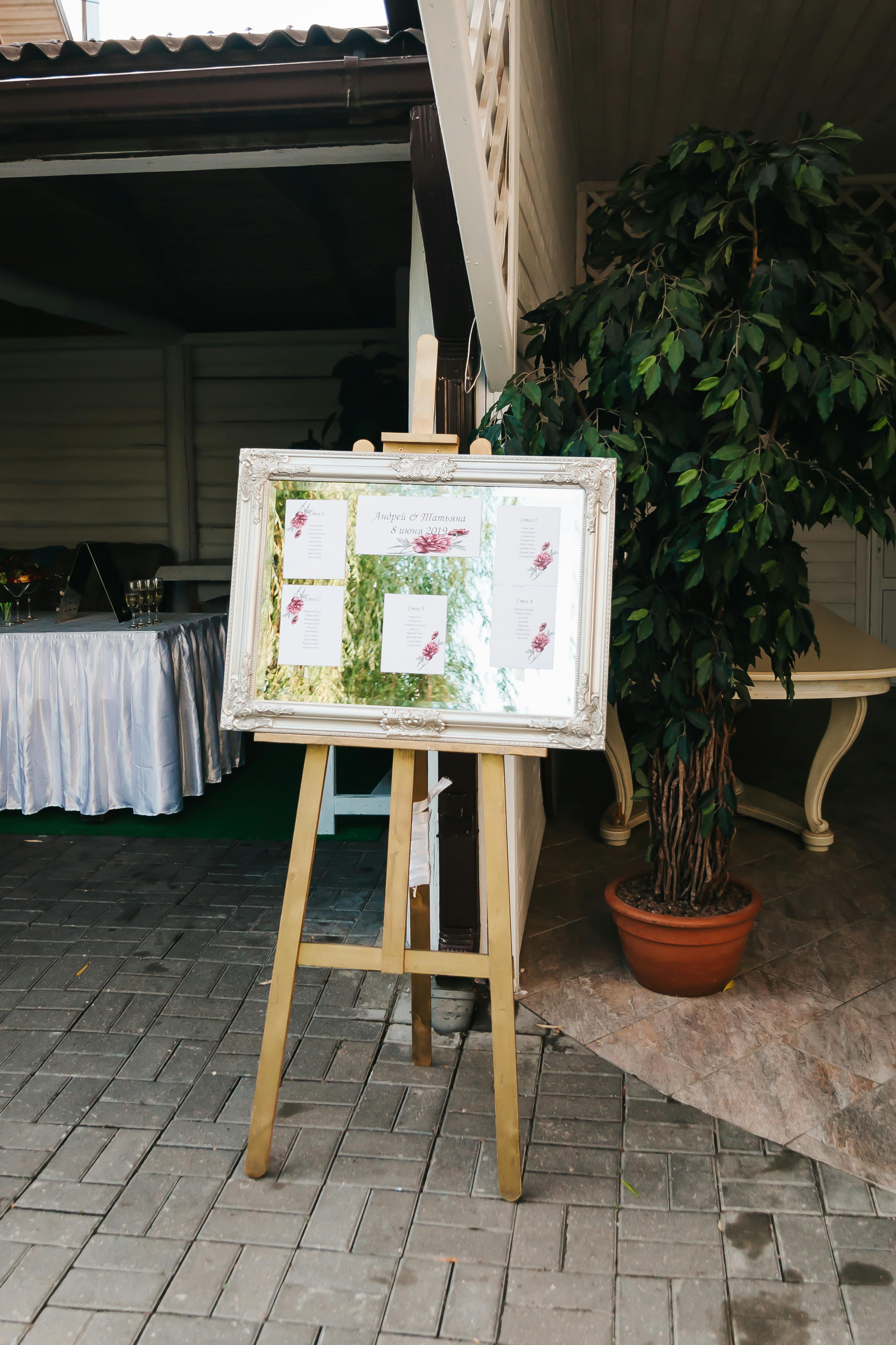 A stylish wedding seating chart on an easel with lush greenery in an elegant venue.