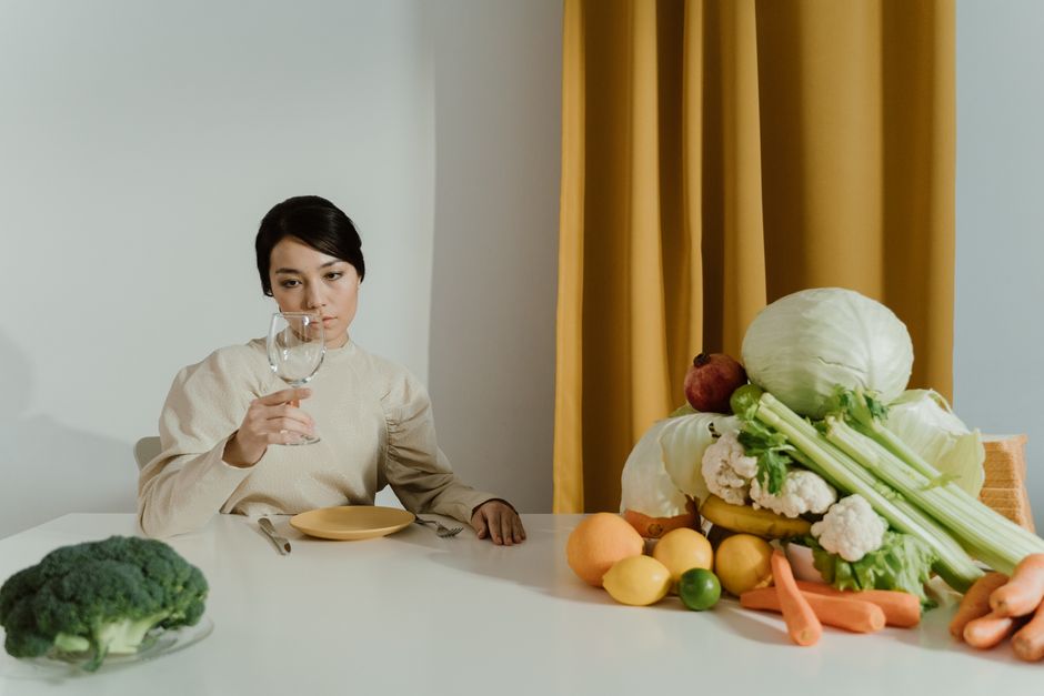 A woman sitting at a table with fresh vegetables, contemplating a wine glass.