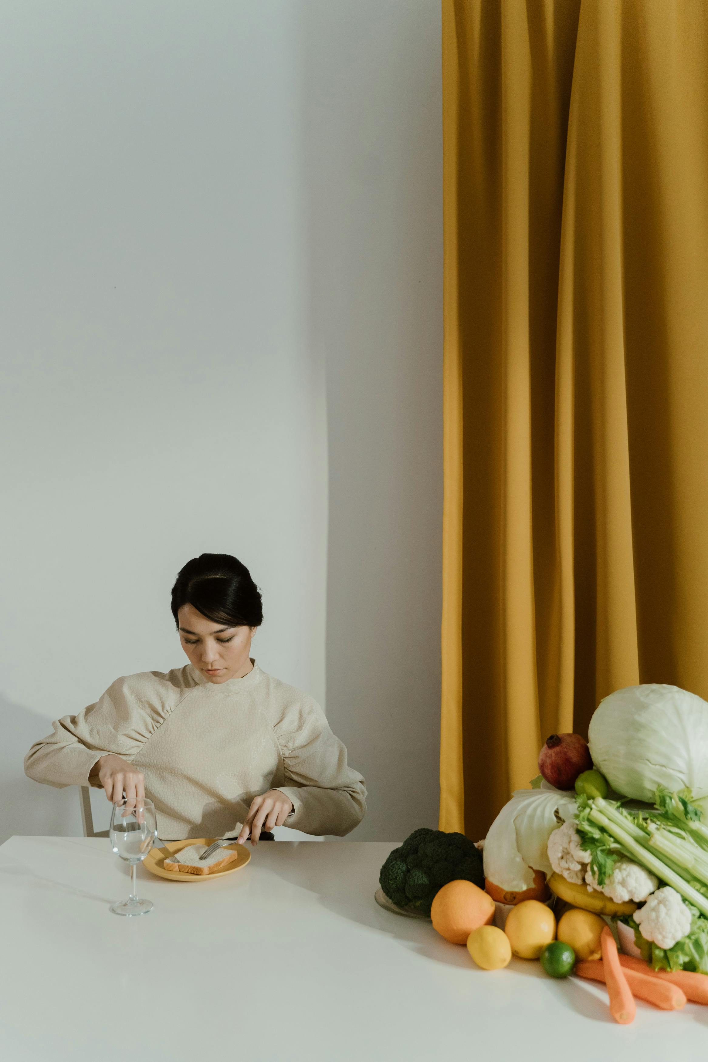 A woman sits at a table with a variety of fresh vegetables, capturing a moment of healthy lifestyle indoors.
