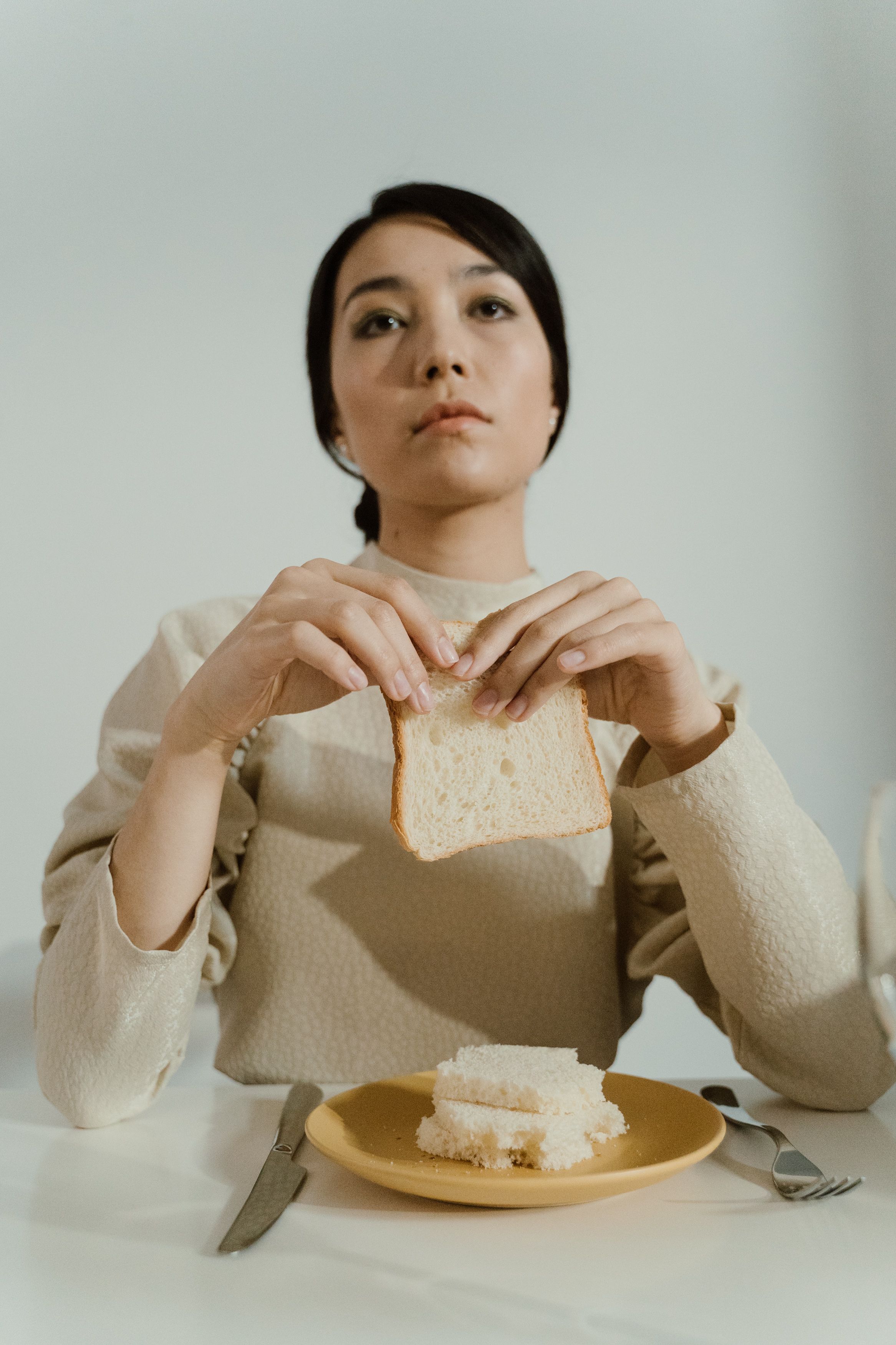 여성이 테이블에 앉아 빵을 들고 있으며, 깊은 생각에 잠긴 듯한 분위기를 자아냅니다.