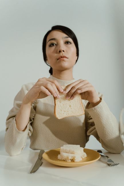 여성이 테이블에 앉아 빵을 들고 있으며, 깊은 생각에 잠긴 듯한 분위기를 자아냅니다.