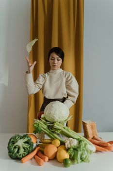 Woman elegantly tosses a cabbage leaf in a minimalist setting with fresh vegetables.